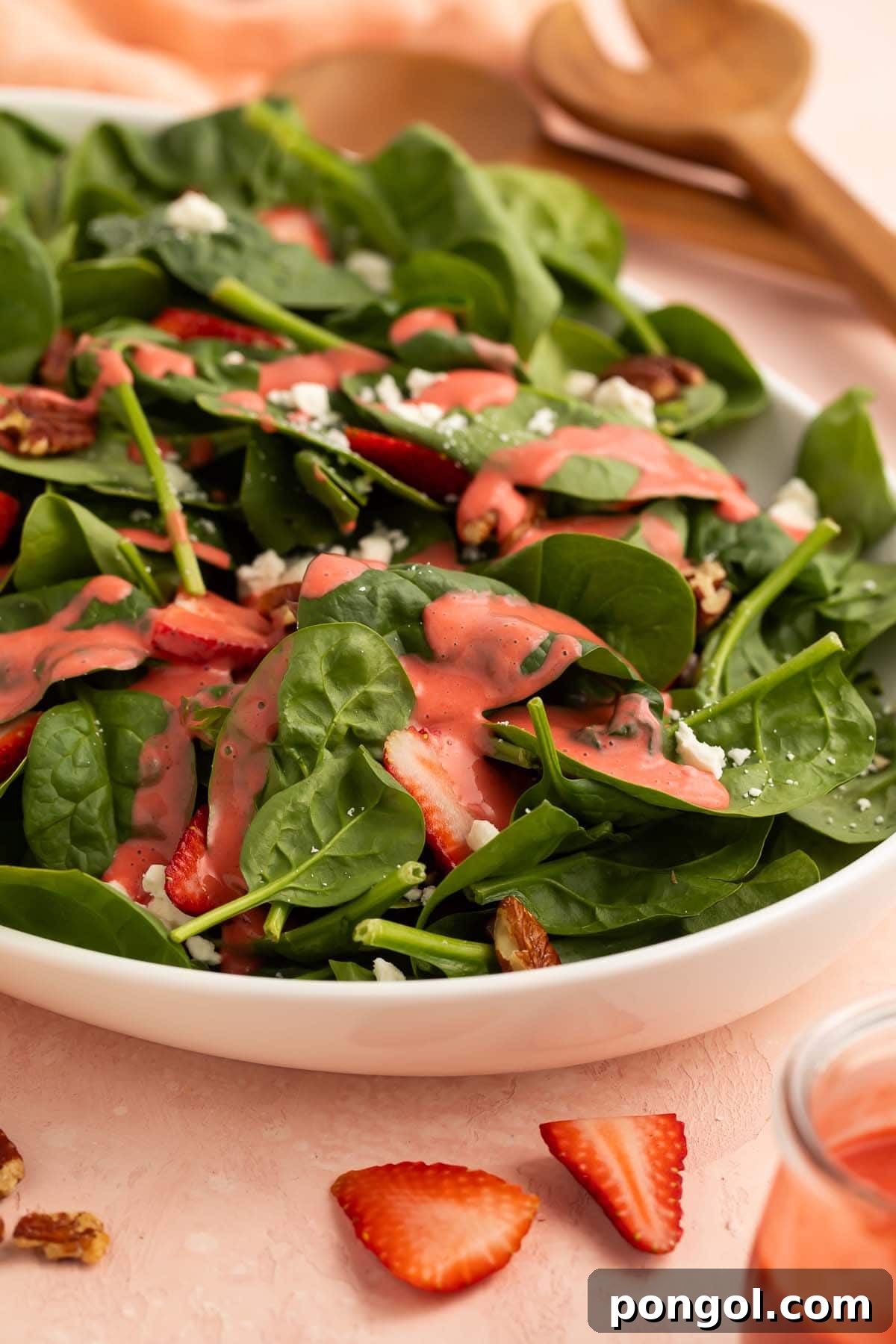 Pale red strawberry vinaigrette drizzled generously over a leafy green spinach salad in a bowl on a table, ready to be enjoyed as a refreshing meal.