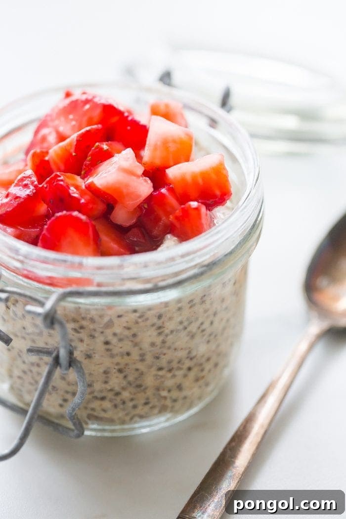 A close-up shot of the best PB&J chia pudding in a glass jar, showing layers of creamy chia pudding and vibrant red macerated strawberries, ready to be enjoyed as a healthy breakfast.