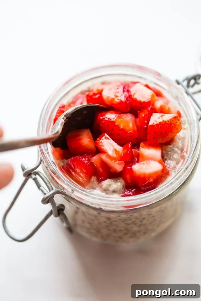 Two glass jars of creamy PB&J chia pudding topped with fresh, macerated strawberries, showcasing the delicious layers and inviting texture. Ideal for a make-ahead vegan breakfast.