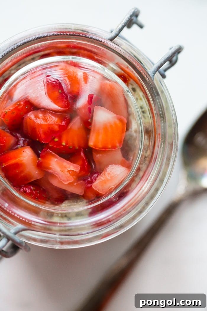 A top-down view of a single serving of PB&J chia pudding in a mason jar, garnished with a whole strawberry and a spoon, emphasizing its grab-and-go convenience and delicious appeal.