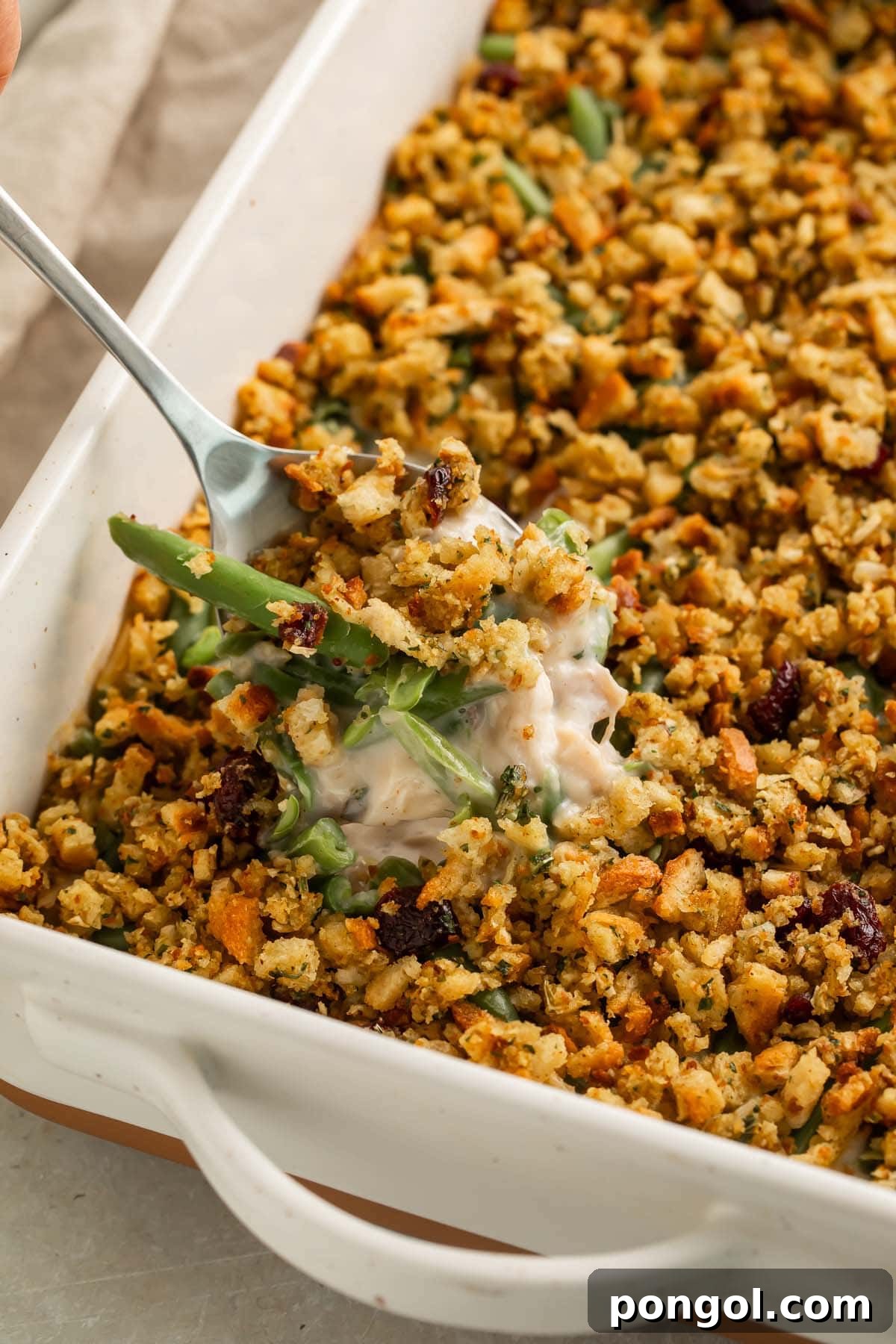 A scoop of creamy chicken and stuffing casserole being lifted out of a casserole dish, showing the creamy sauce and green beans inside.