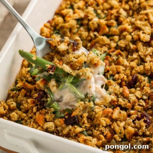 A scoop of creamy chicken and stuffing casserole being lifted out of a casserole dish, showing the creamy sauce and green beans inside.