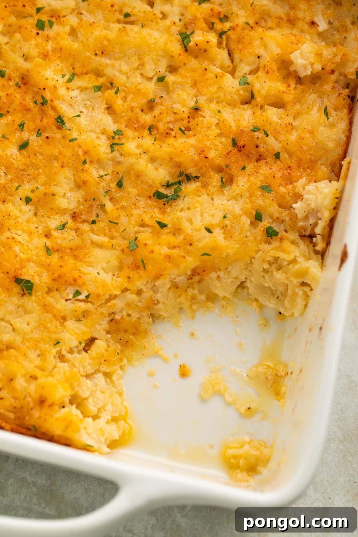A large spoonful of creamy cheesy potato casserole, with melted cheese and soft potatoes, removed from a square white casserole dish.