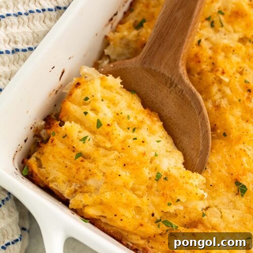 A large wooden spoon resting in a square casserole dish holding a cheesy potato casserole.