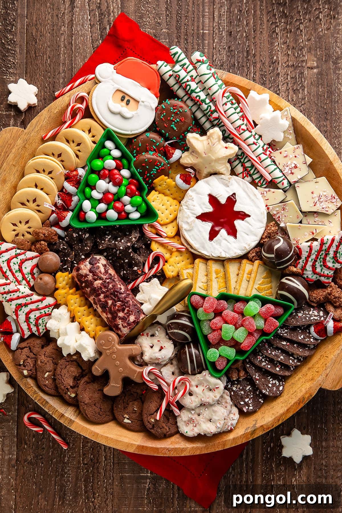 A Christmas dessert themed grazing board, packed full with Christmas tree cakes, brie, goat cheese, crackers, pretzels, truffles, nuts, cookies, and other holiday-themed treats.