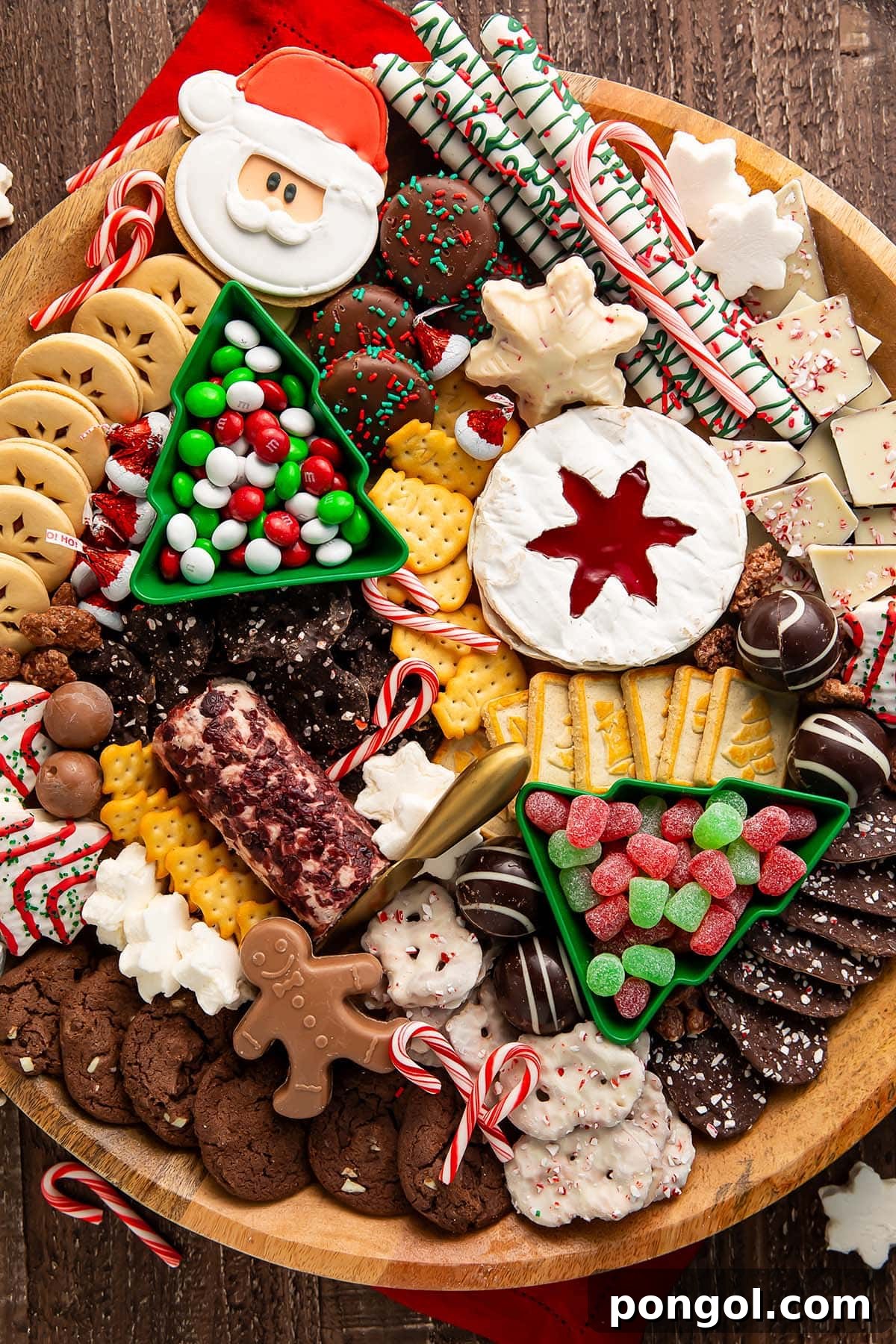 A Christmas dessert themed grazing board, packed full with Christmas tree cakes, brie, goat cheese, crackers, pretzels, truffles, nuts, cookies, and other holiday-themed treats.