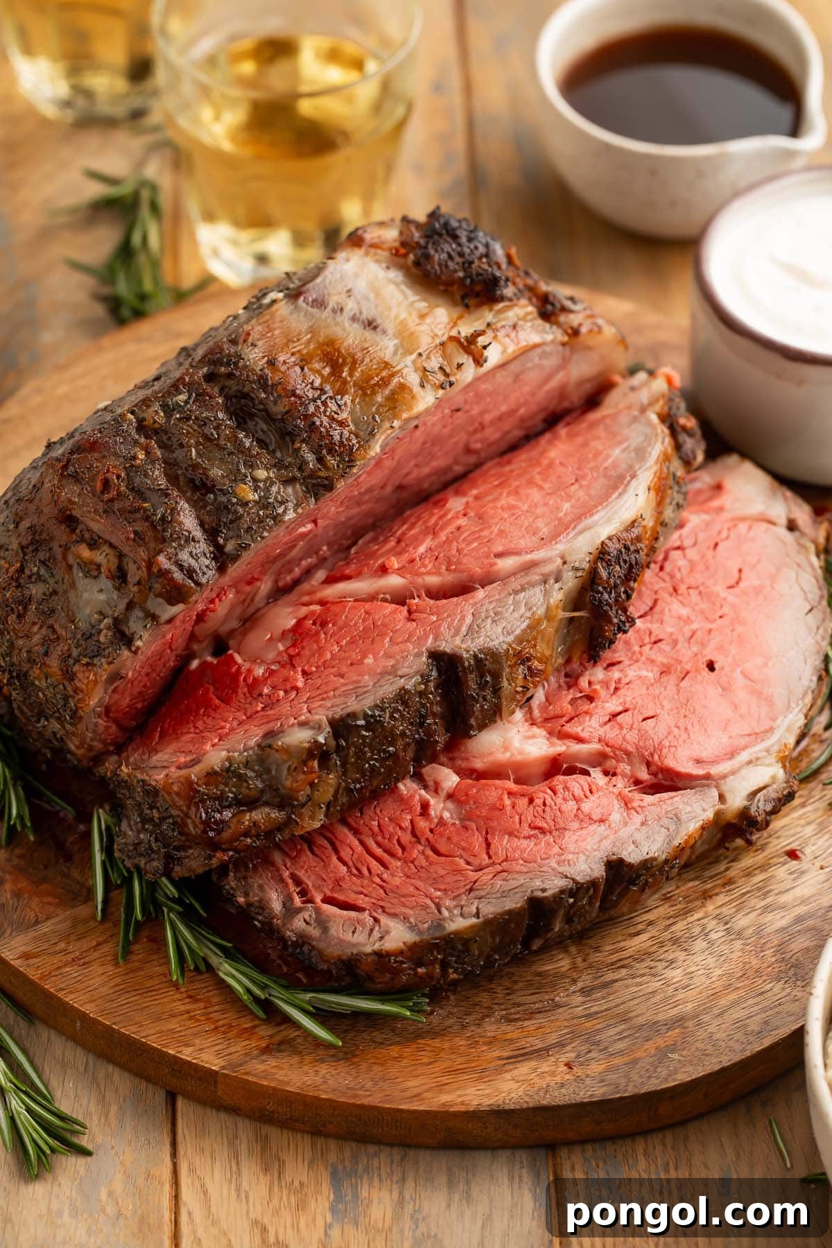 The Perfect Reverse Sear Prime Rib 2 A thickly-carved reverse sear prime rib on a wooden cutting board next to prepared horseradish sauce and au jus.