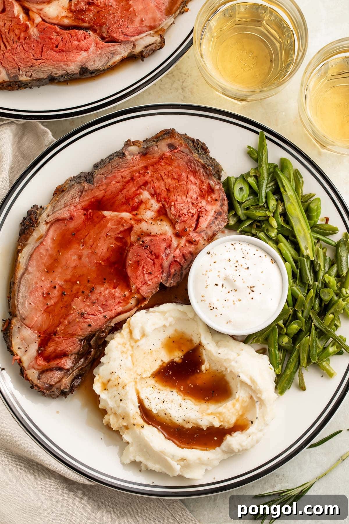 The Perfect Reverse Sear Prime Rib 3 Overhead photo of a plate round white plate with a dark border. On the plate rests a slice of reverse sear prime rib, a scoop of mashed potatoes and gravy, green beans, and horseradish sauce.