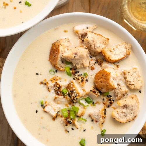 Overhead photo of a bowl of thick, creamy everything bagel chicken soup, topped with sliced green onions and homemade everything bagel croutons.