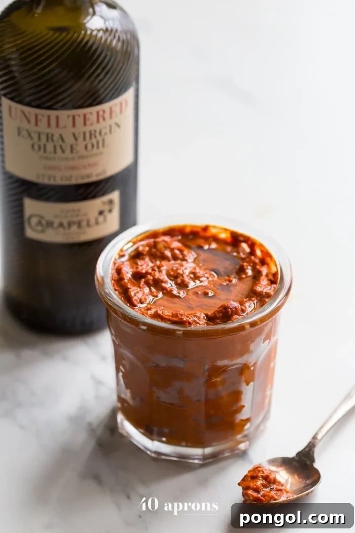 Homemade harissa in a small glass dish with a bottle of Carapelli olive oil in the background, showcasing its rich texture and color