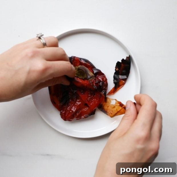 A perfectly roasted red bell pepper being peeled, revealing its tender, sweet flesh for the harissa paste