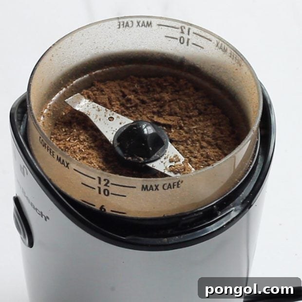 Whole spices being finely ground into a powder in a spice mill, ready to infuse flavor into the harissa