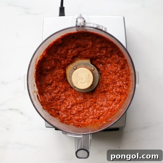 Homemade harissa spice paste beautifully blended in the bowl of a food processor, showcasing its smooth texture