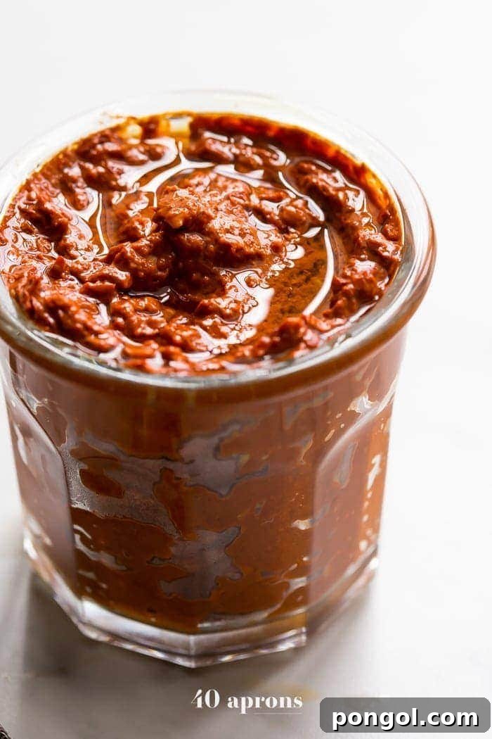 Close-up of a small glass dish filled with homemade harissa spice paste, highlighting its vibrant red hue and smooth consistency