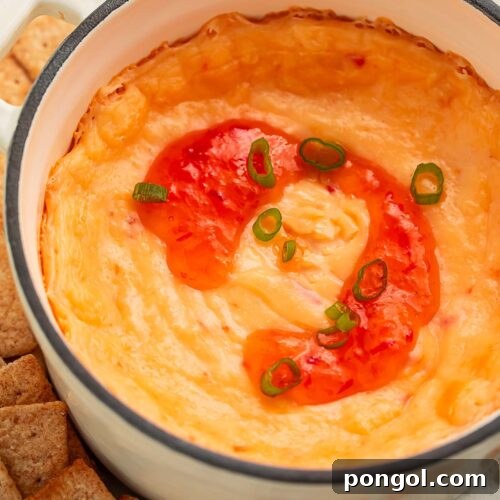 A high-sided bowl of cream cheese pepper jelly dip topped with a swirl of red pepper jelly, surrounded by square wheat crackers.