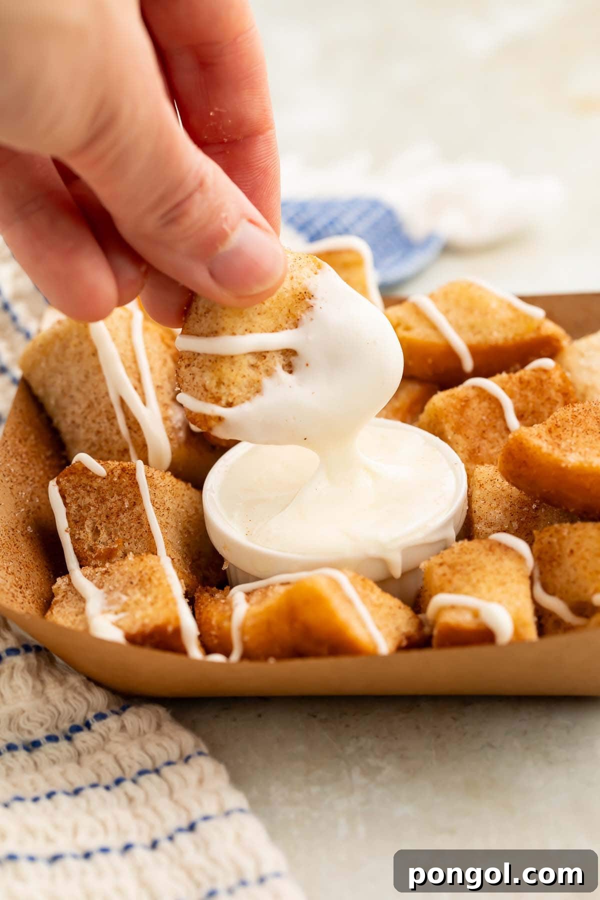 A white woman's hand holding one of the keto cinnamon roll bites, dipping it into a small ramekin of cream cheese icing, highlighting the delicious texture and dipping experience.