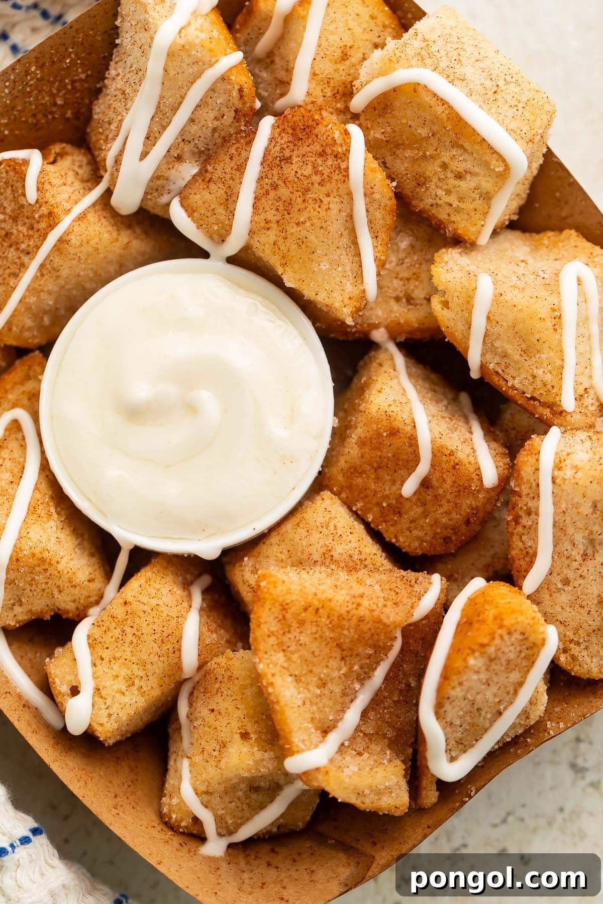 Close-up detailed shot of a cardboard tray holding multiple keto cinnamon roll bites, showcasing their perfectly golden-brown exterior and the rich cream cheese icing in a ramekin beside them.