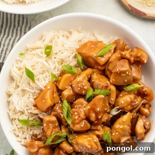 Overhead photo of a bowl of Instant Pot bourbon chicken with white rice garnished with sliced green onions.