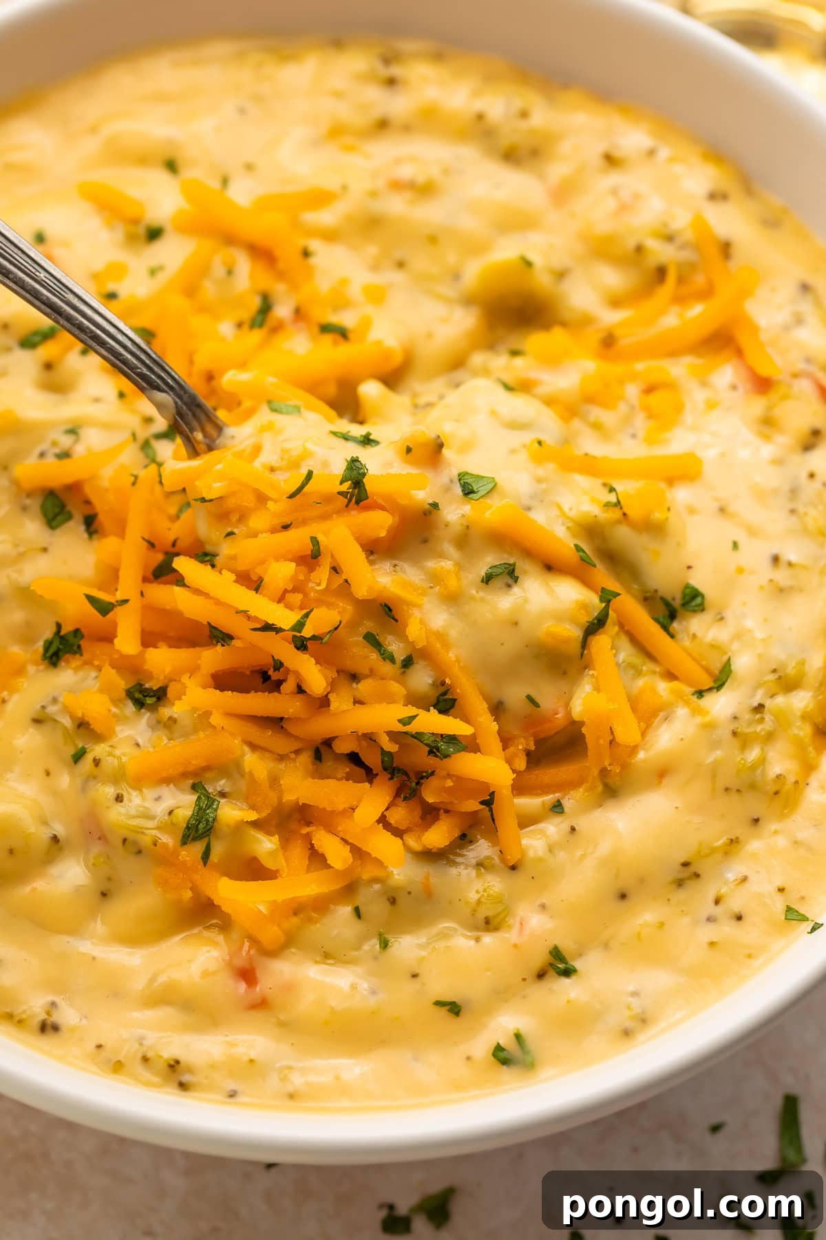 Close up of vegan broccoli soup with spoon showing creamy texture and cheese garnish