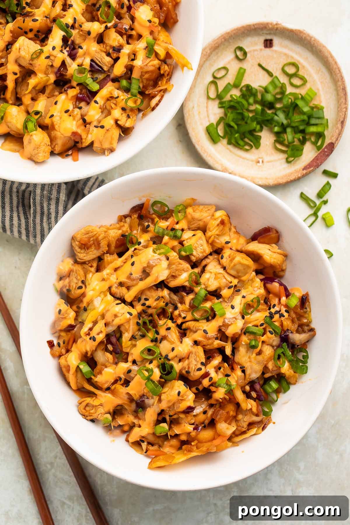 Two bowls of chicken egg roll in a bowl on a table, garnished with green onions and sesame seeds.