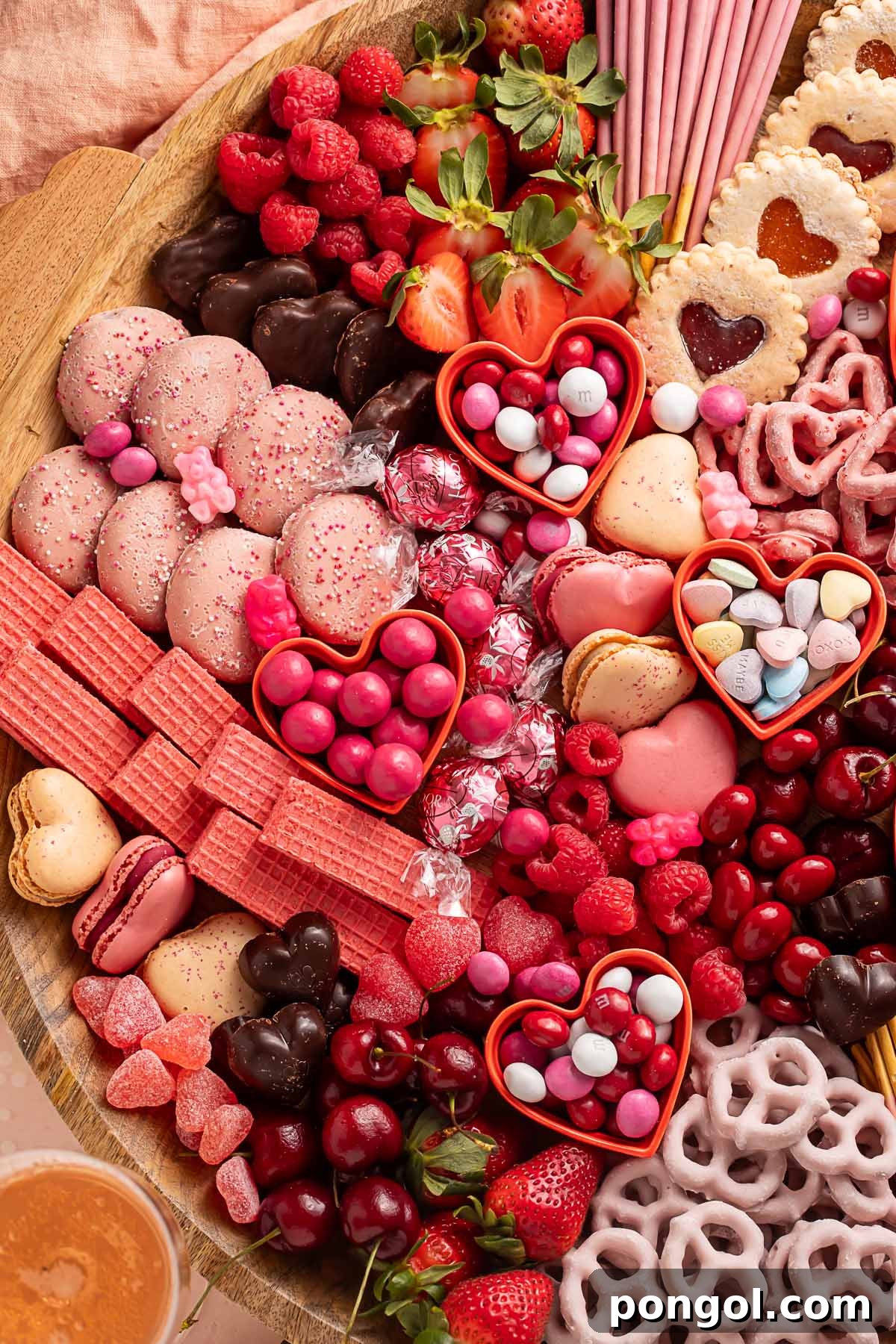 Cupid's Sweetest Board 4 A Valentine's Day themed charcuterie board filled with pink, red, and white cookies, candies, pretzels, fruits, and chocolates, showcasing a delightful arrangement.