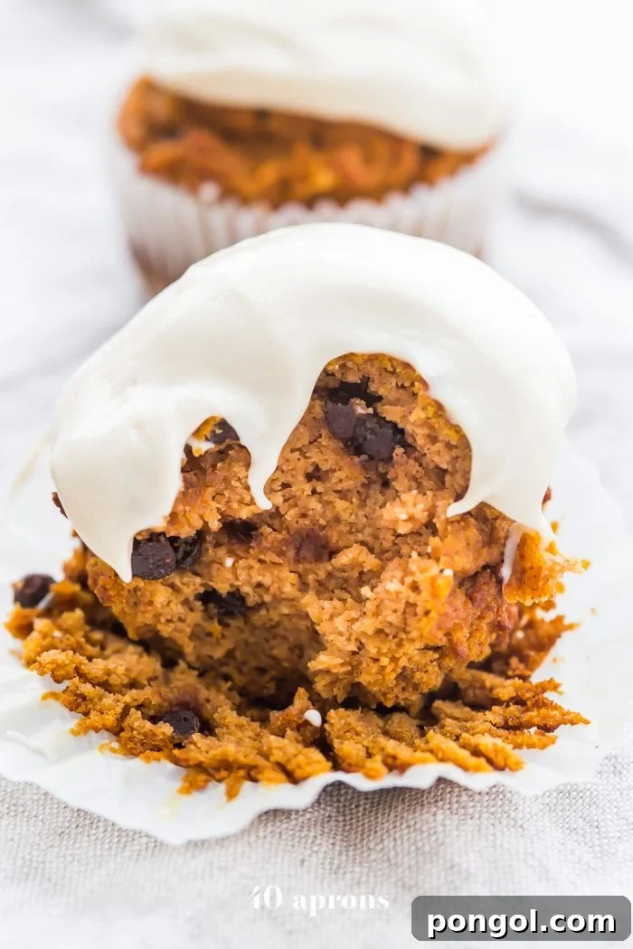 Delicious Paleo Pumpkin Chocolate Chip Muffins with Cream Cheese Frosting on a wooden board, showcasing their moist texture and generous frosting.