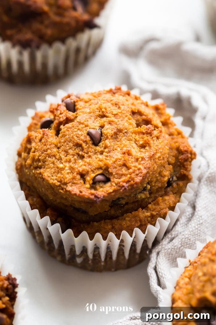 A stack of freshly baked Paleo Pumpkin Chocolate Chip Muffins, generously topped with creamy, sweet-tangy frosting.