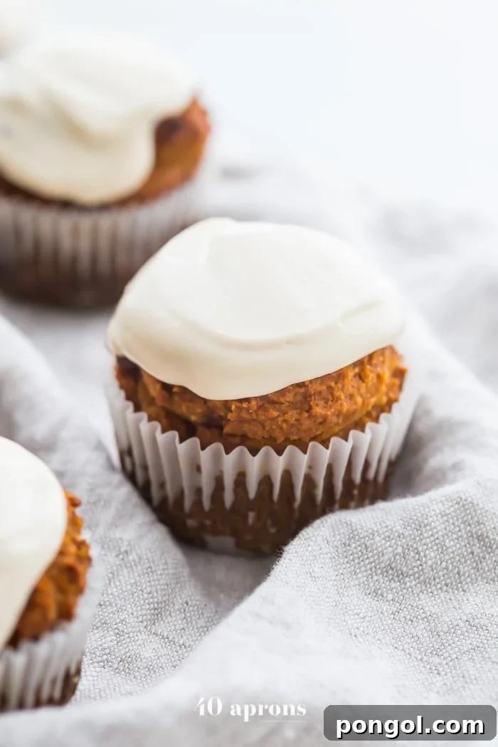 Hand holding a perfectly frosted Paleo Pumpkin Chocolate Chip Muffin, ready to be enjoyed as a healthy fall treat.