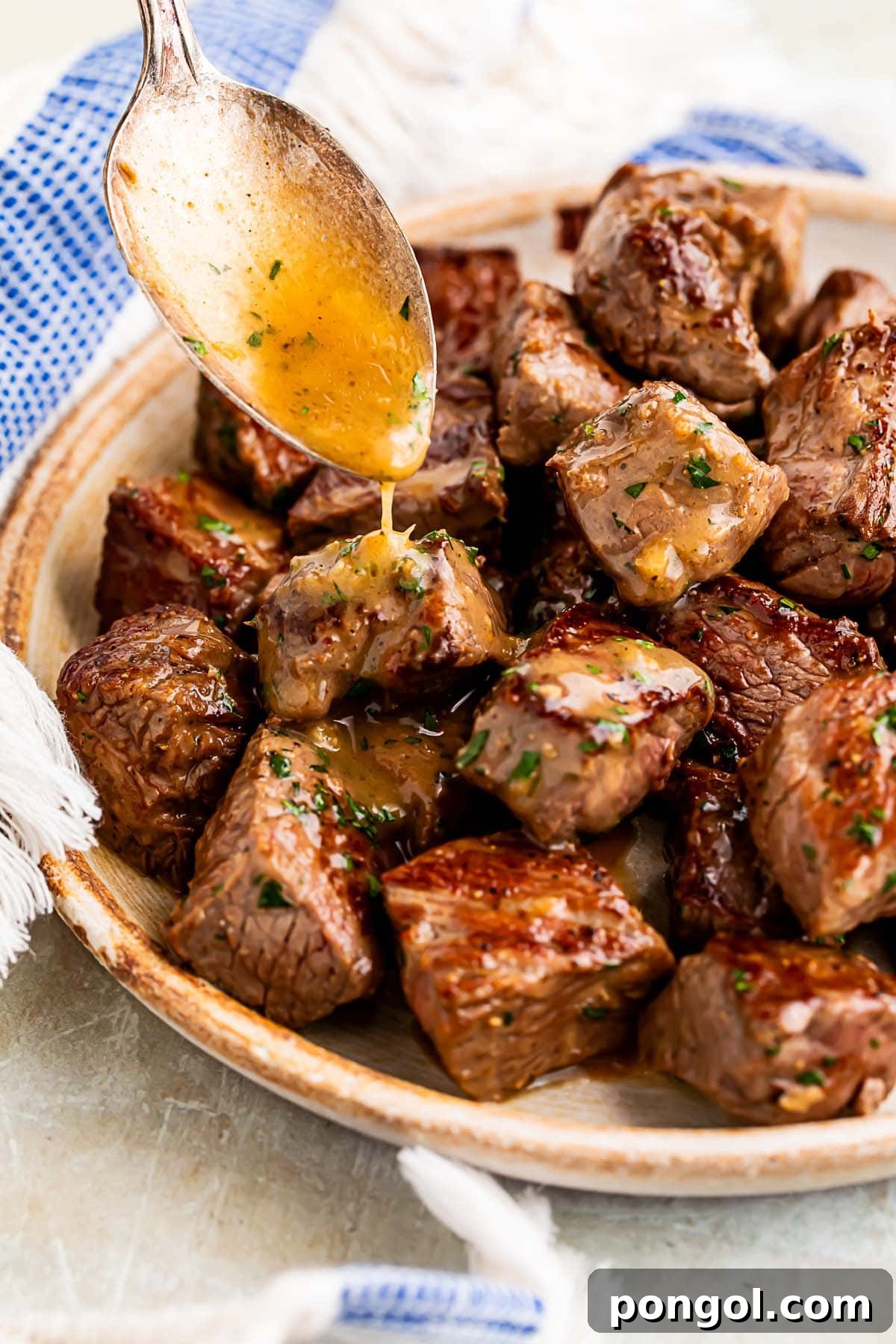 Garlic butter being spooned over steak bites in a large bowl, glistening with flavor.
