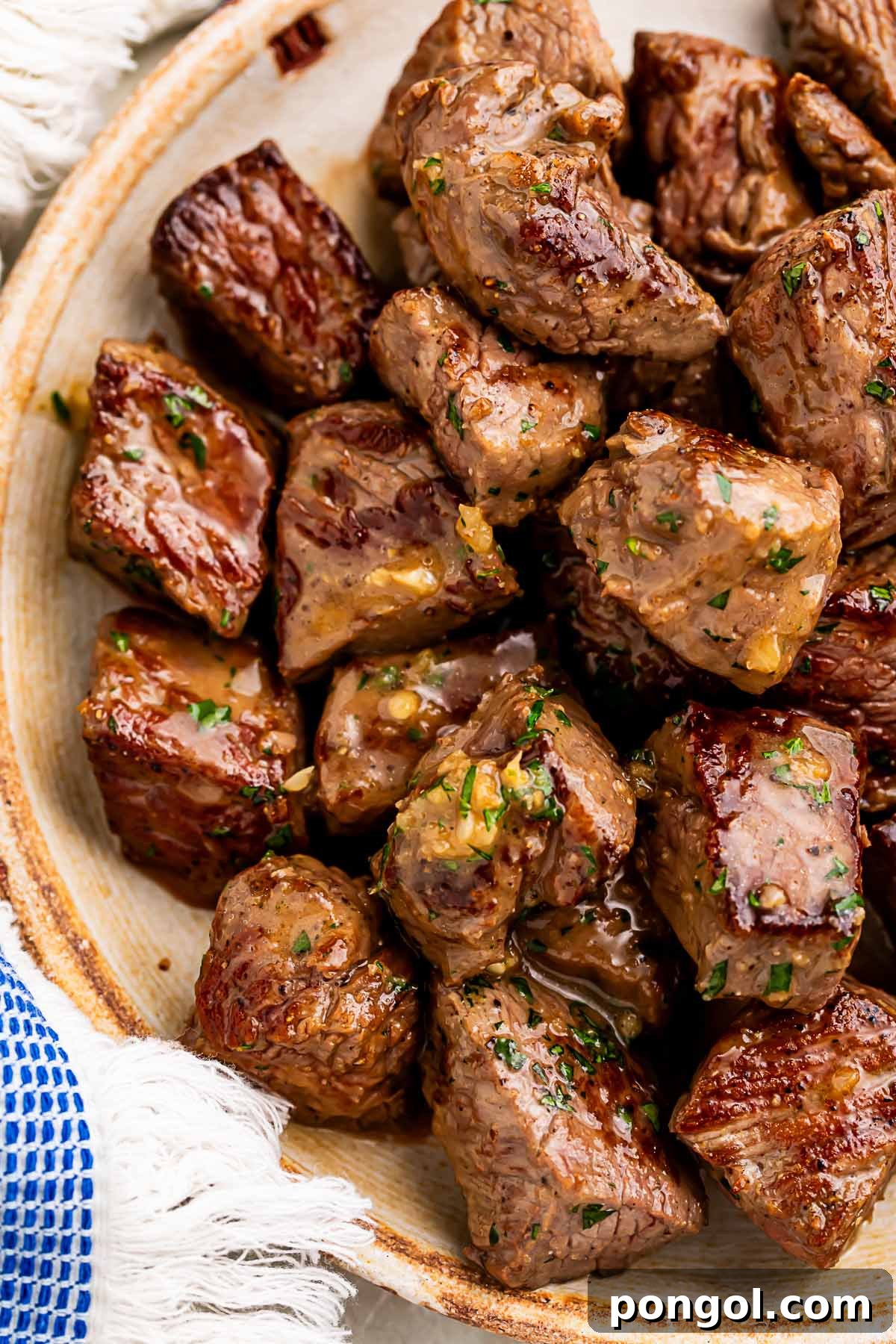 A large bowl of garlic butter steak bites next to a blue and white kitchen towel, ready to serve.