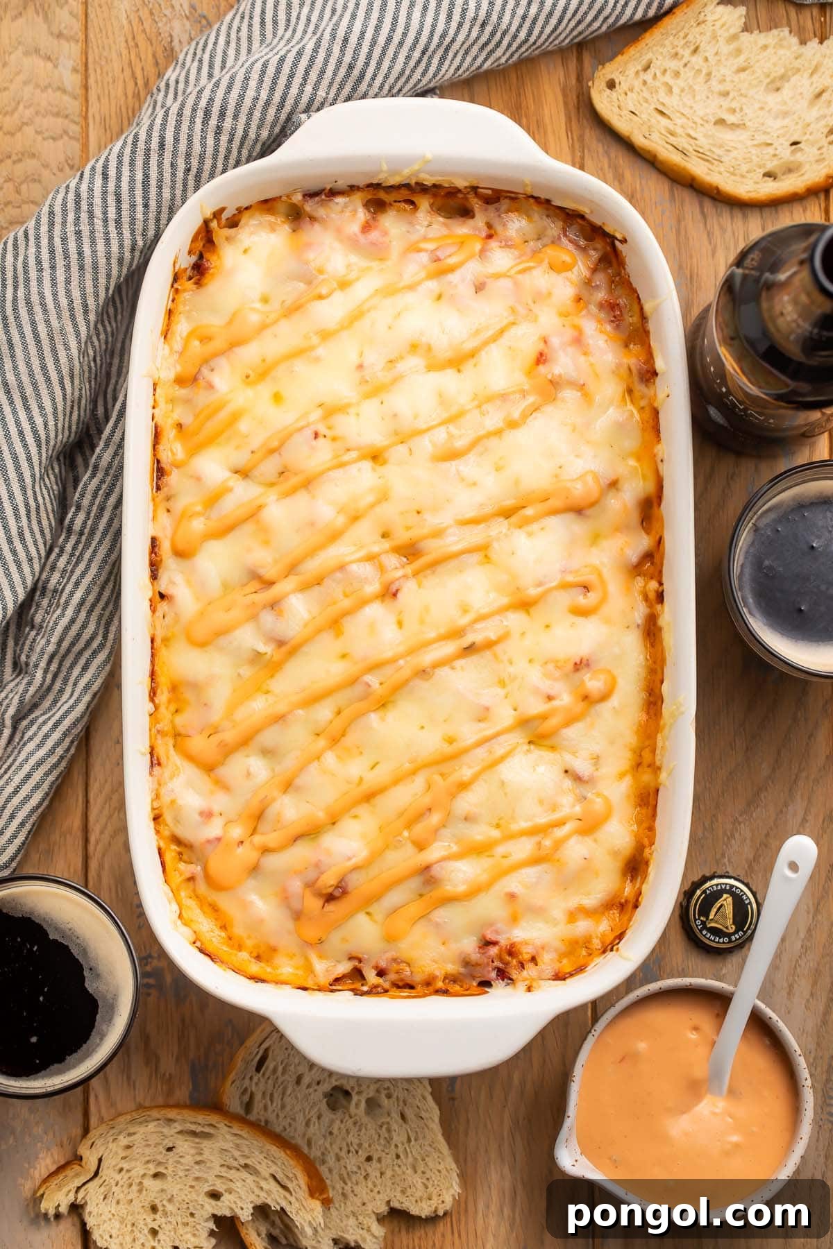 Overhead photo of a delicious Reuben casserole on a rustic wooden table, surrounded by a bowl of Russian dressing and slices of fresh rye bread, ready to be served.
