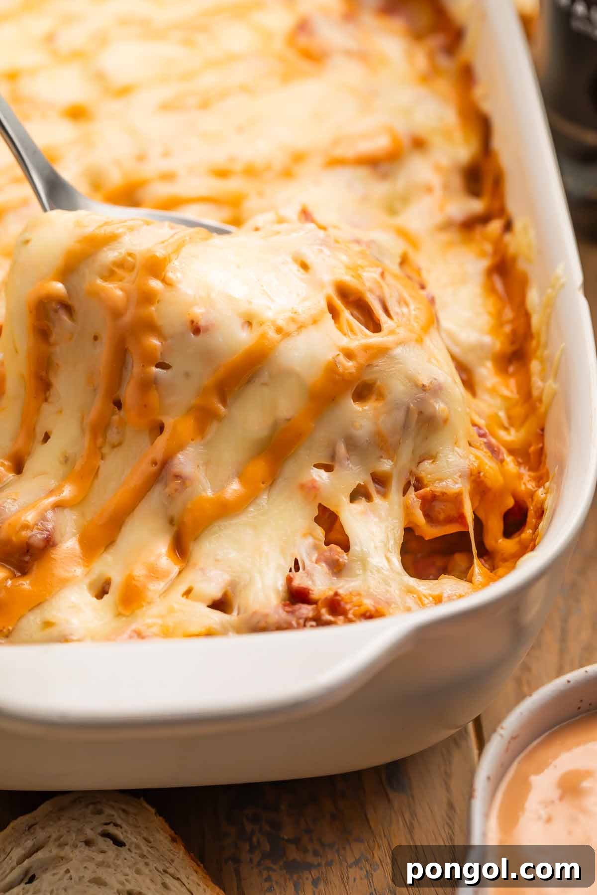 A serving spoon lifting a portion of hot, cheesy Reuben casserole from the dish, highlighting the delicious layers.