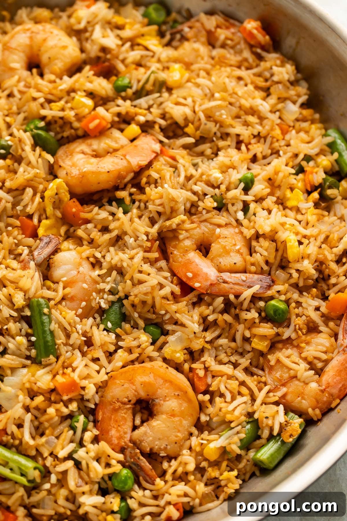 Golden Shrimp Fried Rice Feast 2 A large silver skillet holding fully-prepared shrimp fried rice with large juicy shrimp, green beans, and peas littered throughout.