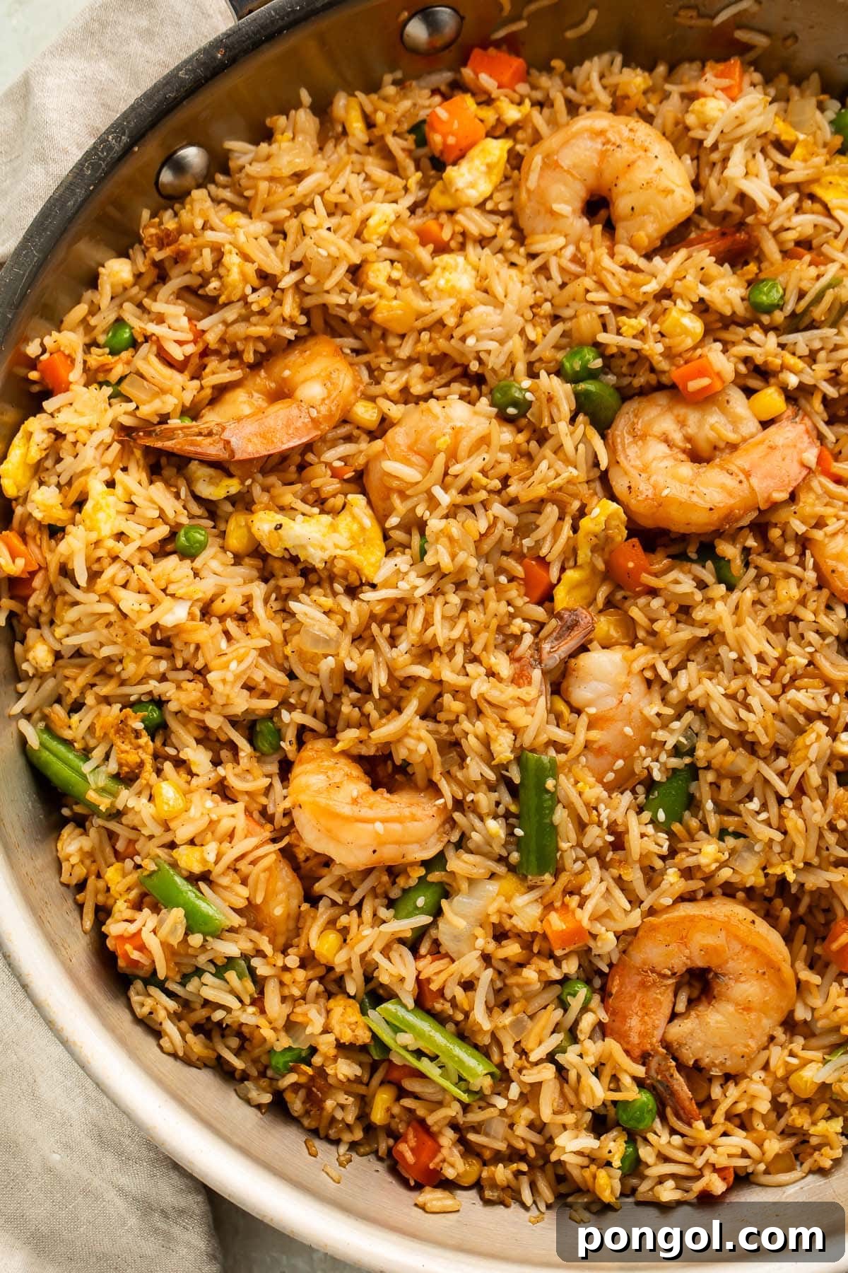 Golden Shrimp Fried Rice Feast 3 A large silver skillet holding fully-prepared shrimp fried rice with large juicy shrimp, green beans, and peas littered throughout.