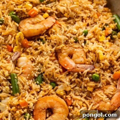 A large silver skillet holding fully-prepared shrimp fried rice with large juicy shrimp, green beans, and peas littered throughout.