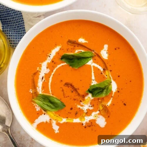 Two bowls of orange tomato soup with cream swirls and fresh herbs