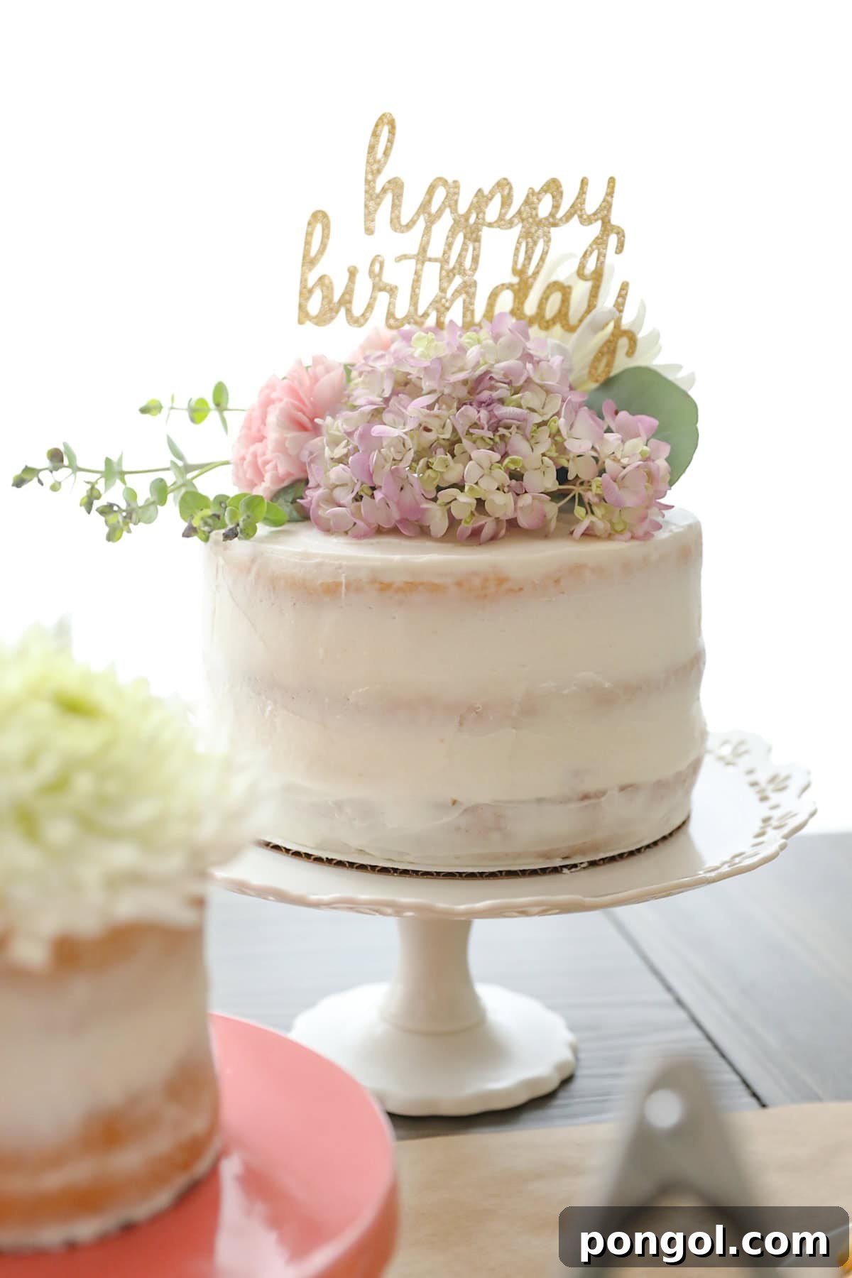 A naked cake topped with fresh flowers and a gold "Happy Birthday" script topper.