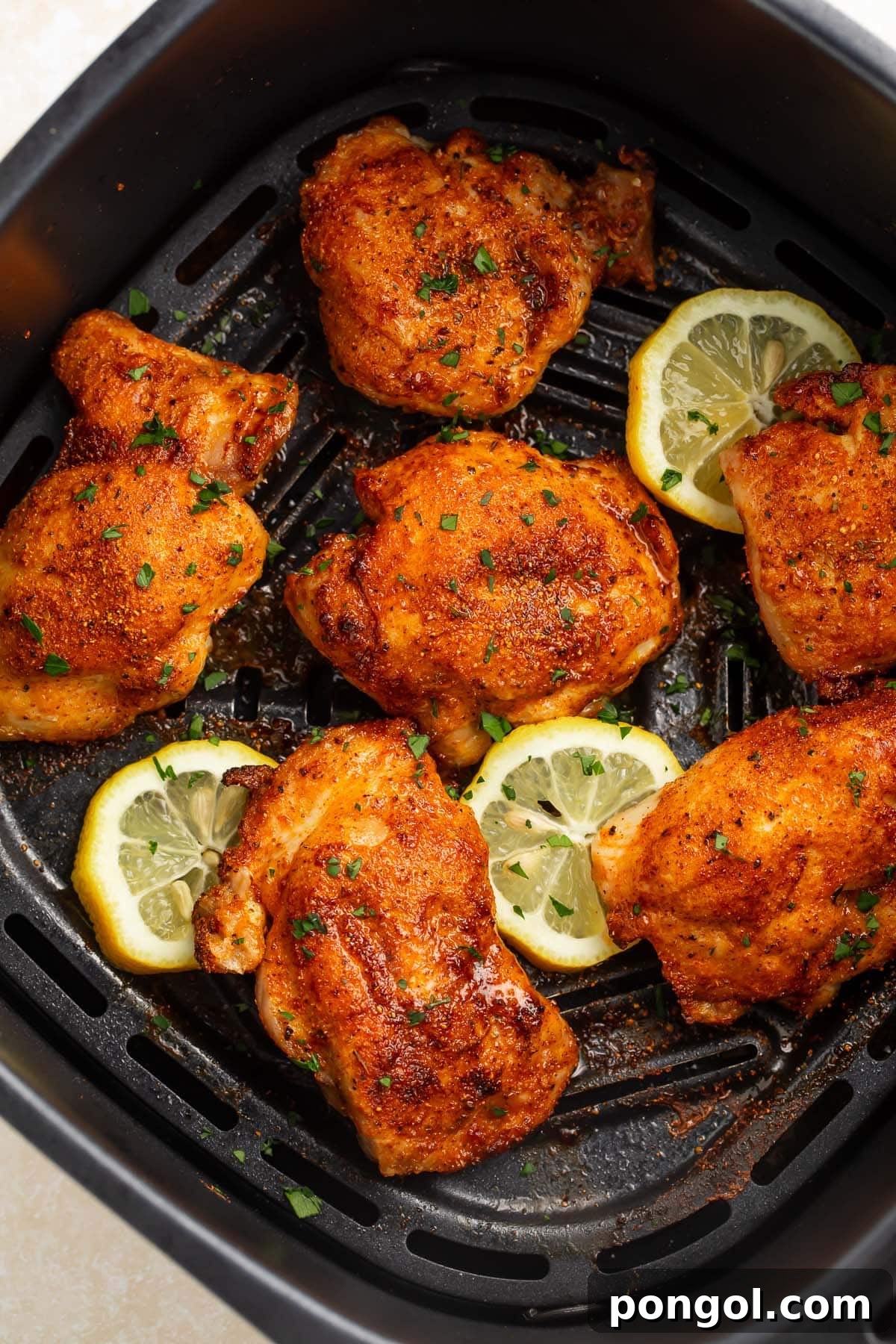 6 boneless, skinless chicken thighs in an air fryer basket with air fried lemon coins.