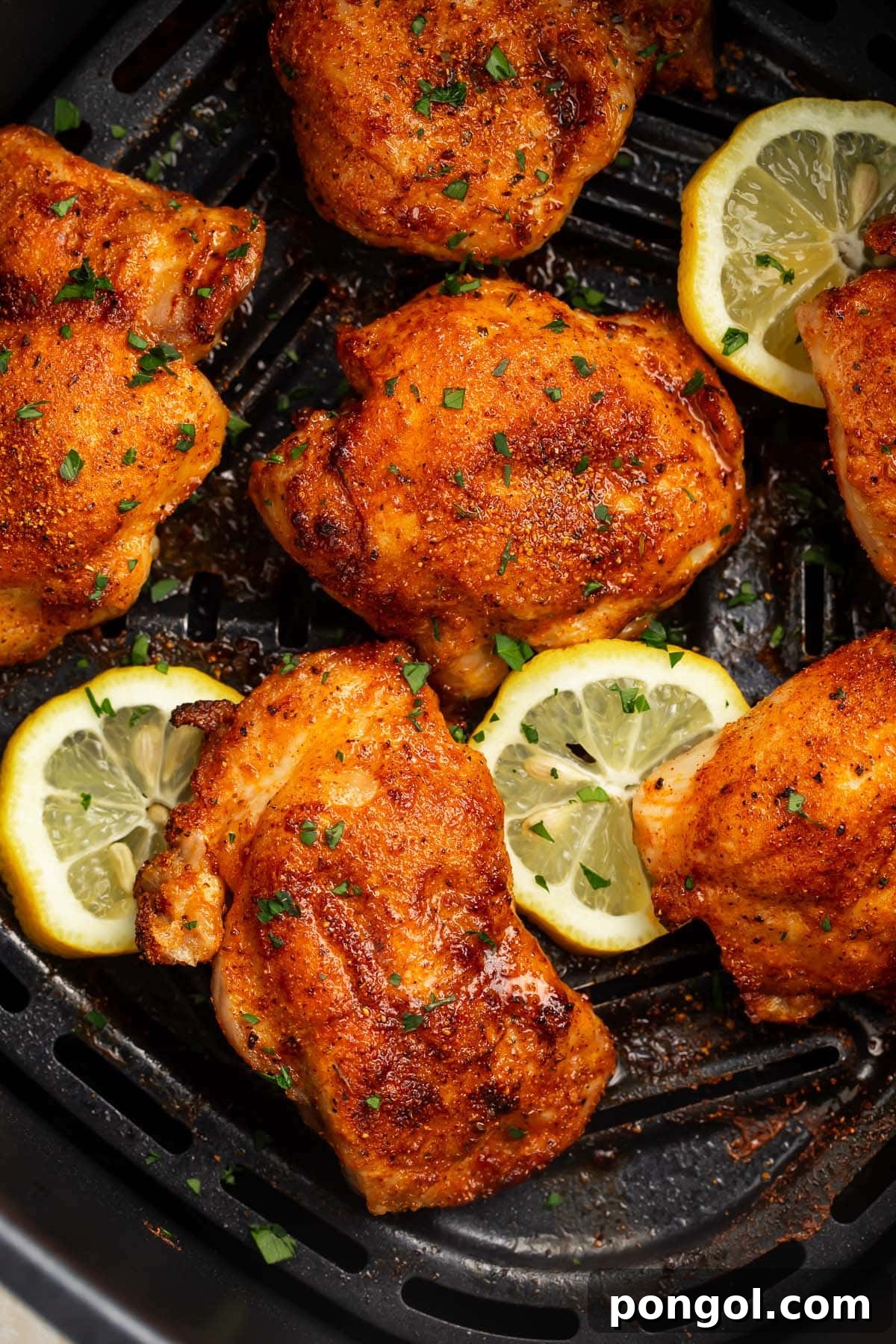 6 boneless, skinless chicken thighs in an air fryer basket with air fried lemon coins.