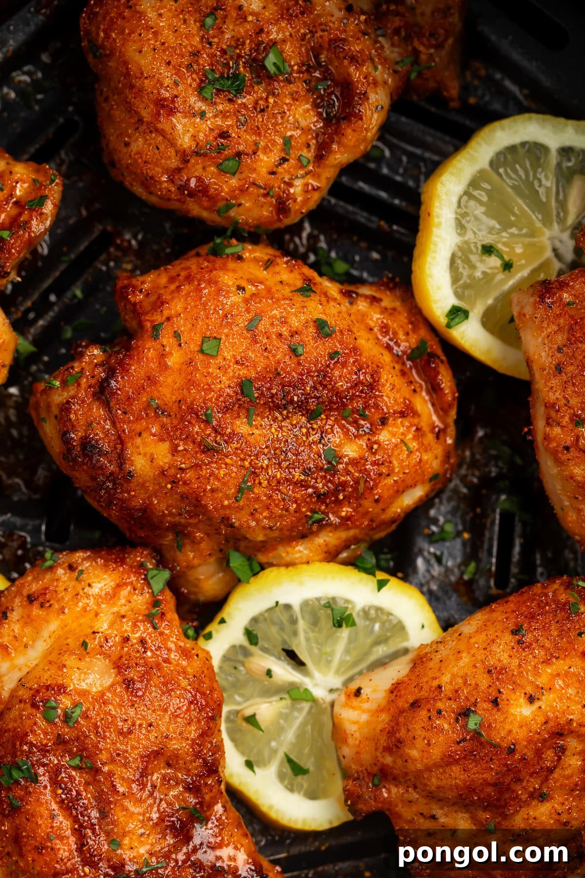 6 boneless, skinless chicken thighs in an air fryer basket with air fried lemon coins.