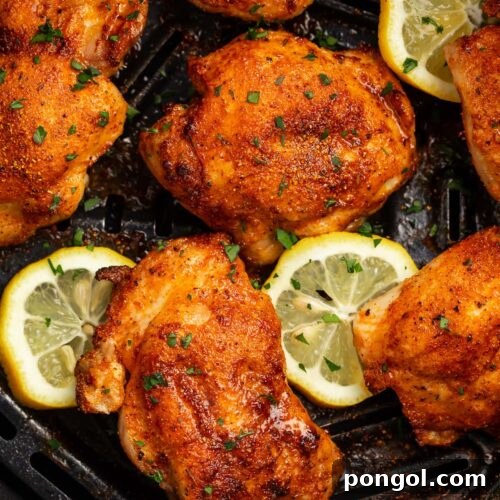 6 boneless, skinless chicken thighs in an air fryer basket with air fried lemon coins.