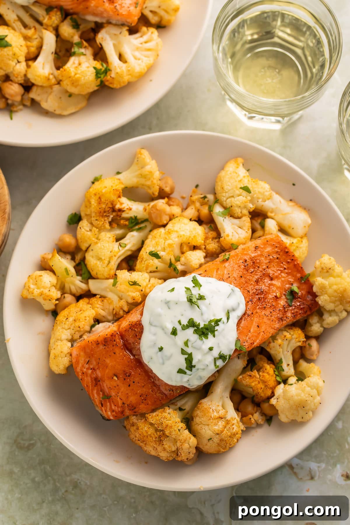 A beautifully presented bowl of hot honey sheet pan salmon and roasted cauliflower, garnished with fresh herbs and a drizzle of yogurt sauce.