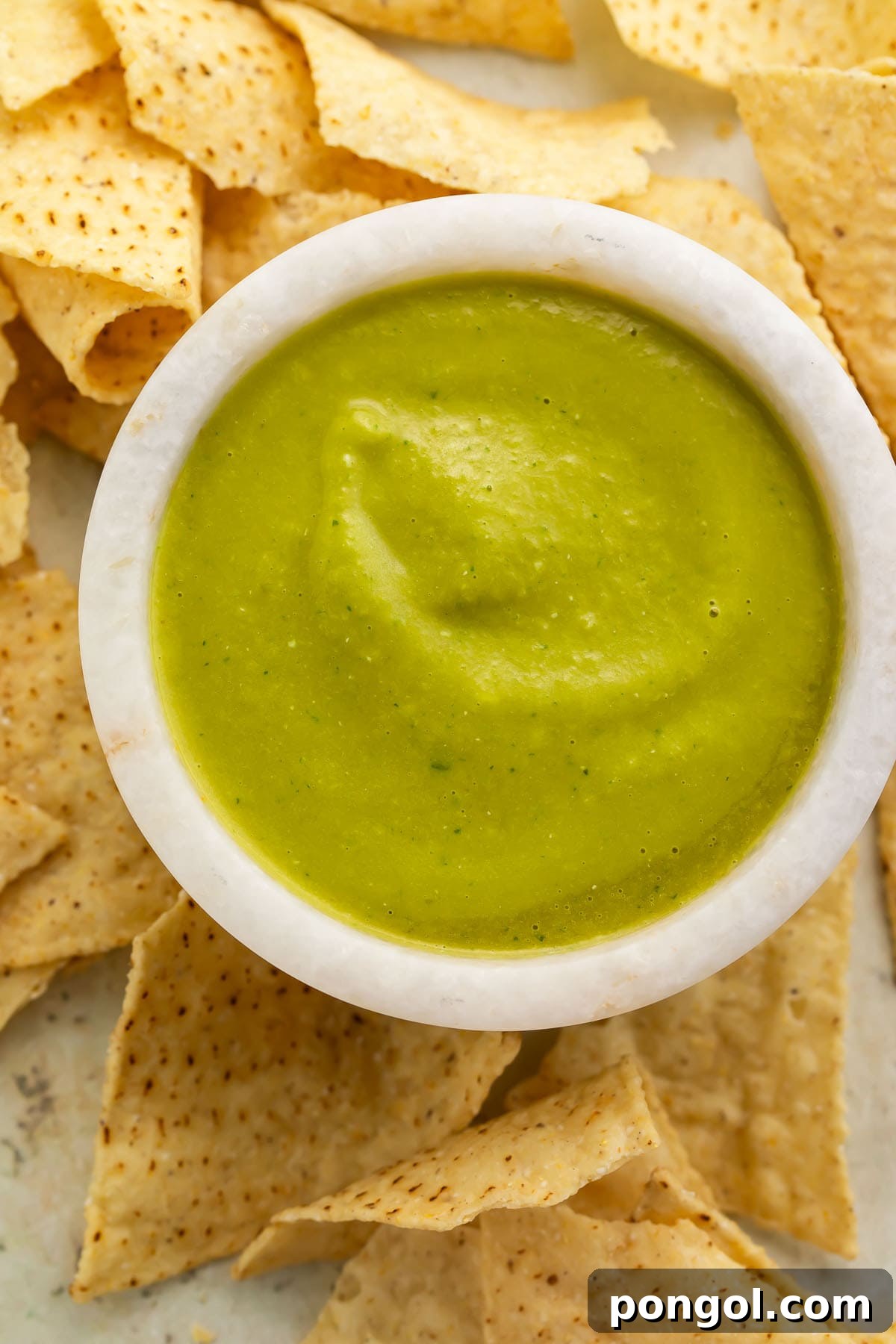 Piquant Jalapeño Salsa 3 Overhead photo of a white stone bowl holding vibrant green jalapeno salsa, surrounded by tortilla chips.
