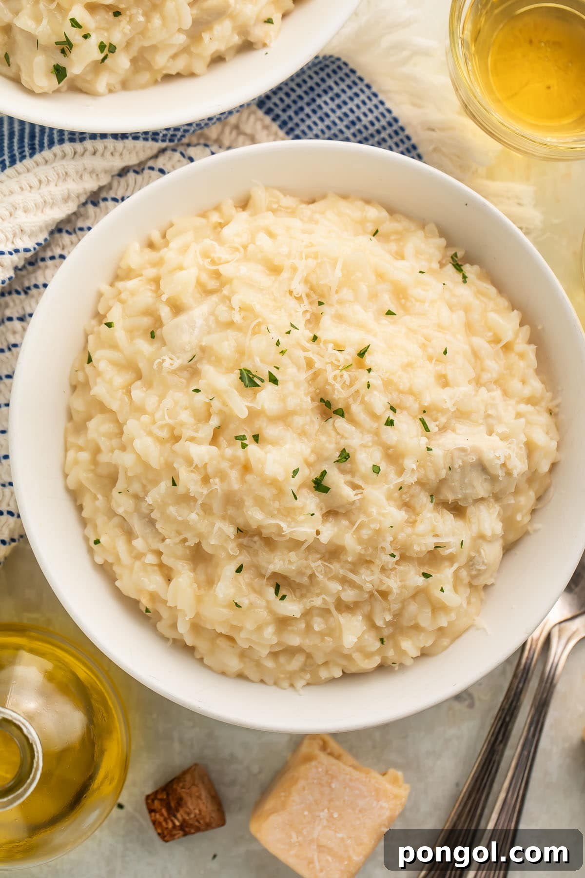 A large white bowl of Instant Pot chicken risotto on a table with a blue and white kitchen towel next to a glass of white wine.