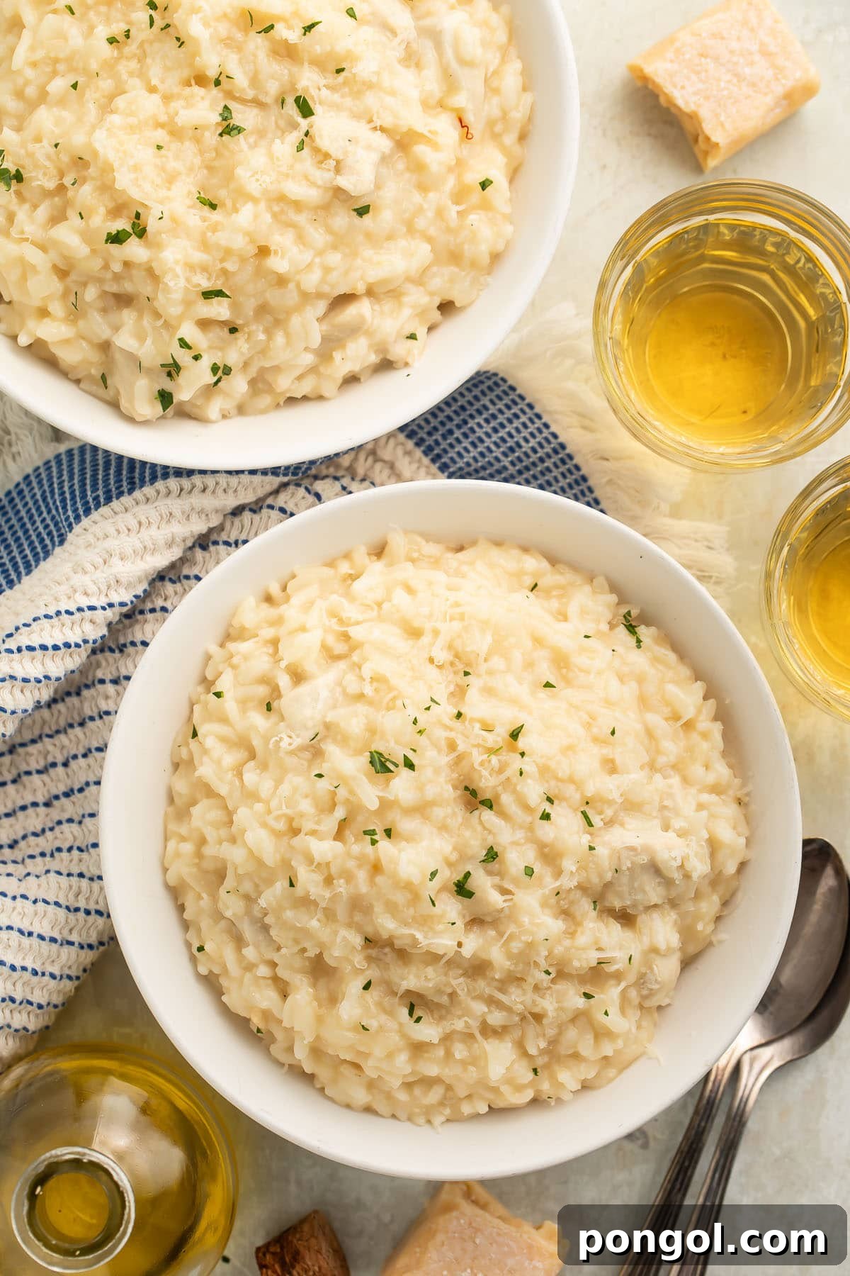 A large white bowl of Instant Pot chicken risotto on a table with a blue and white kitchen towel next to a glass of white wine.