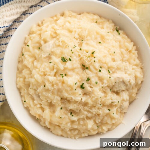 A large white bowl of Instant Pot chicken risotto on a table with a blue and white kitchen towel next to a glass of white wine.