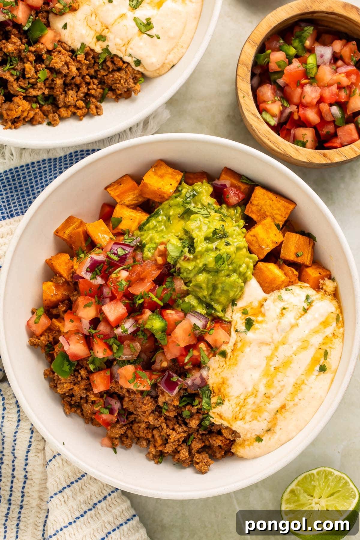 Overhead photo of a vibrant Southwest Ground Beef Bowl with Cottage Cheese Queso, adorned with fresh toppings, sitting on a rustic wooden table.