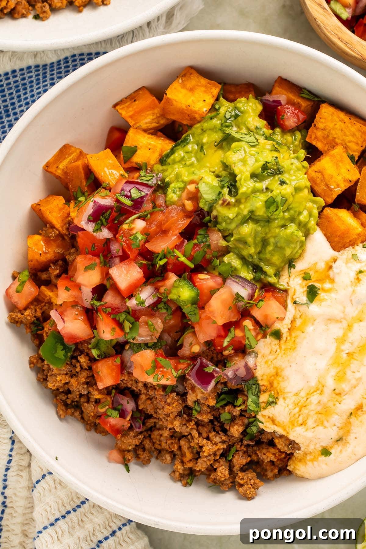 Close-up photo highlighting the texture and layers of a Southwest Ground Beef Bowl with Cottage Cheese Queso, garnished with fresh cilantro and a drizzle of sauce.