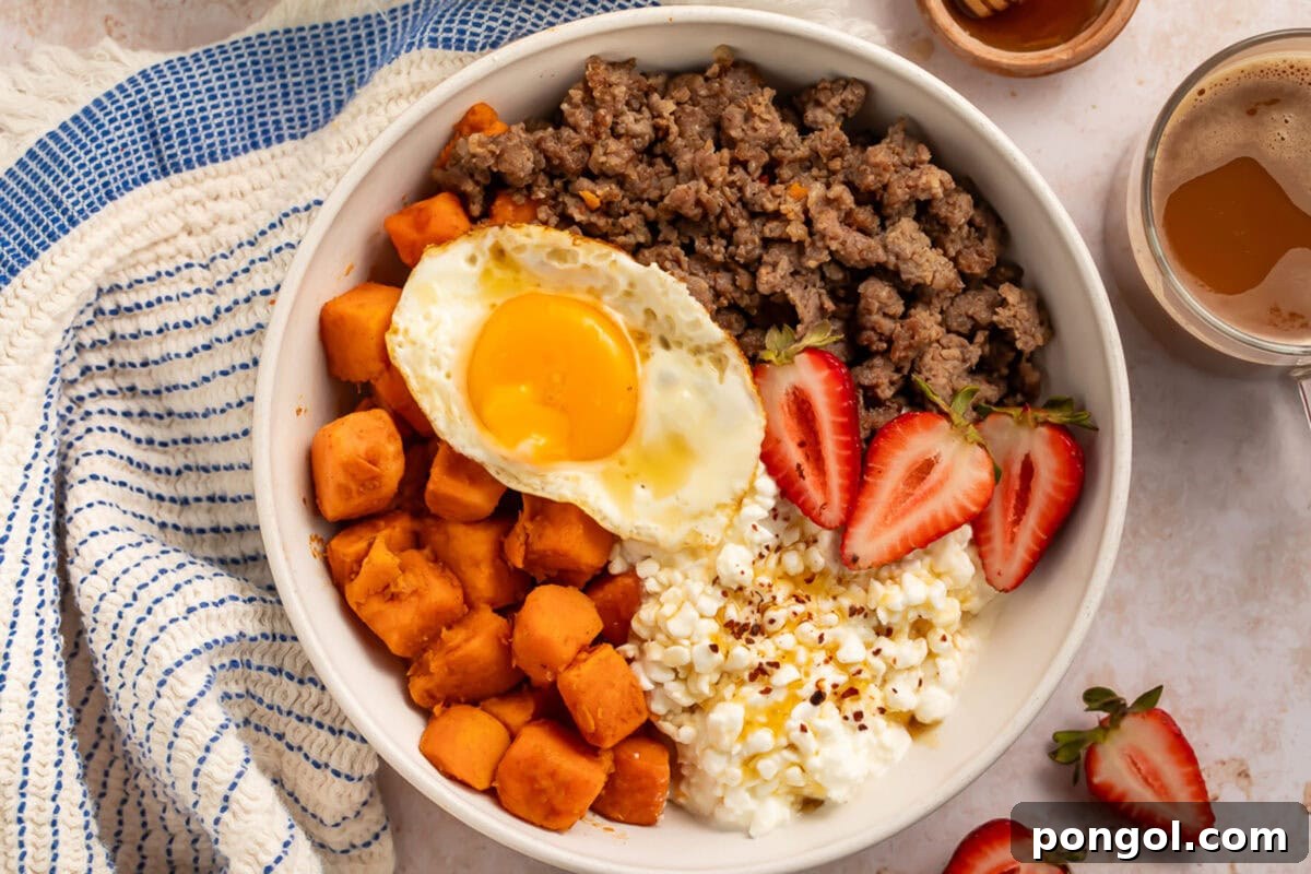A beautifully presented breakfast bowl featuring a base of cottage cheese, topped with golden roasted sweet potatoes, savory breakfast sausage, and garnished with fresh sliced strawberries and a perfectly cooked fried egg.