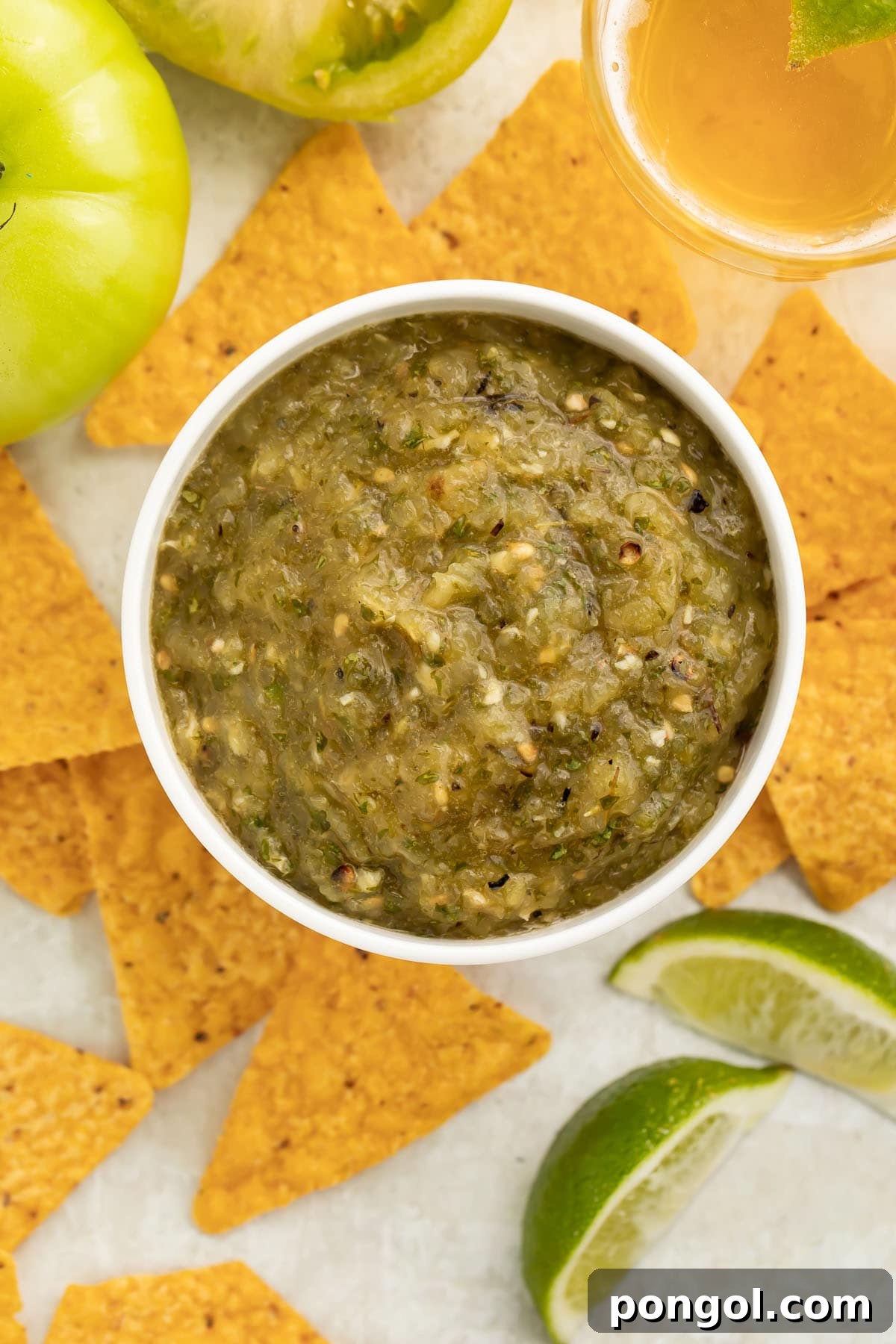 An overhead view of a generously sized bowl filled with chunky green tomato salsa, artfully surrounded by triangular tortilla chips for easy dipping.